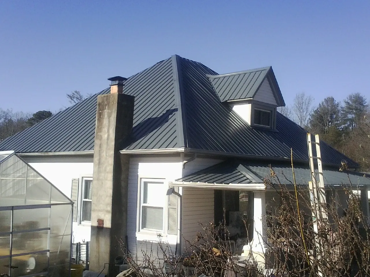 Dark blue standing seam metal roof on a white farmhouse with dormer — Slate & Tile Roof Repair by Roofing Brothers in Lovilia