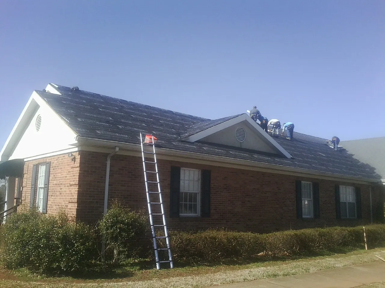 Crew tearing shingles off a brick ranch roof with a ladder set — Metal Roof Repair work by our crew in Lovilia
