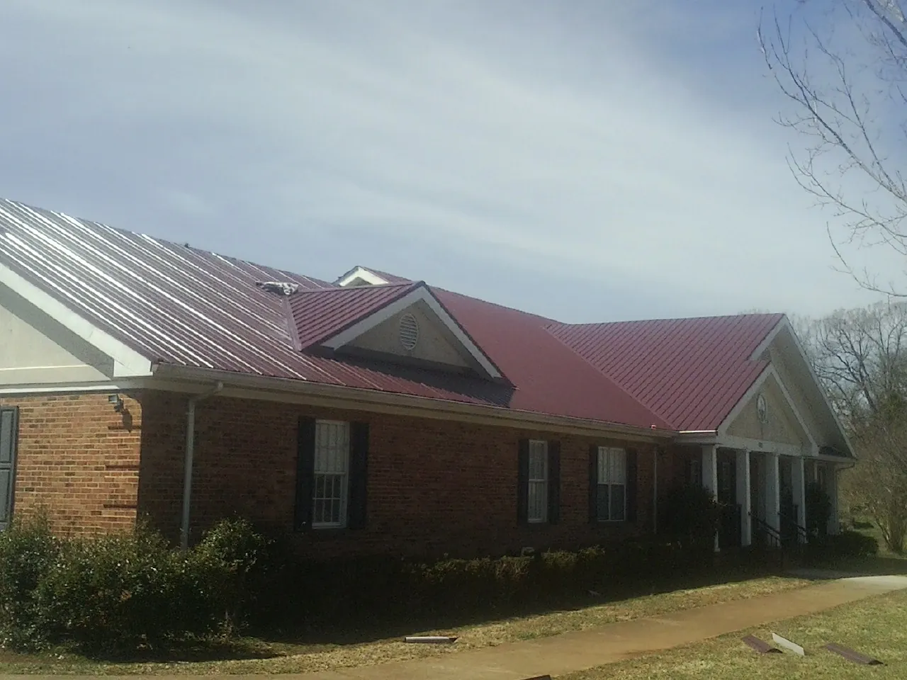 Red metal roof with gabled entries on a long brick building, from a Hail Damage Roof Repair job in Lovilia