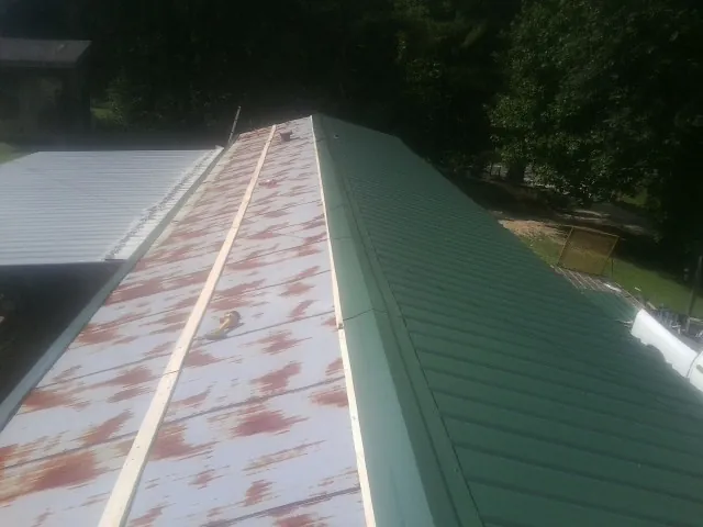 Old rusted panels beside newly installed green metal roofing — Wind Damage Roof Repair by Roofing Brothers in Lovilia