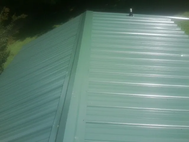 New green metal panels meeting at the ridge of a roof — Flat Roof Repair work by our crew in Lovilia