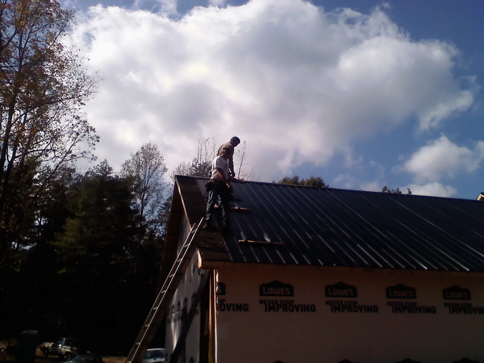 Roofer fastening dark metal panels high against a cloudy sky, from a Roof Inspection job in Lovilia