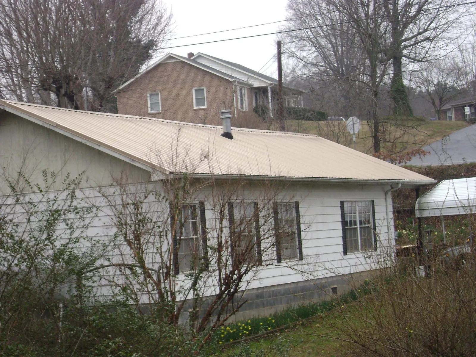 Tan metal roof on a white sided house set into a hillside — Commercial Roofing by Roofing Brothers in Lovilia