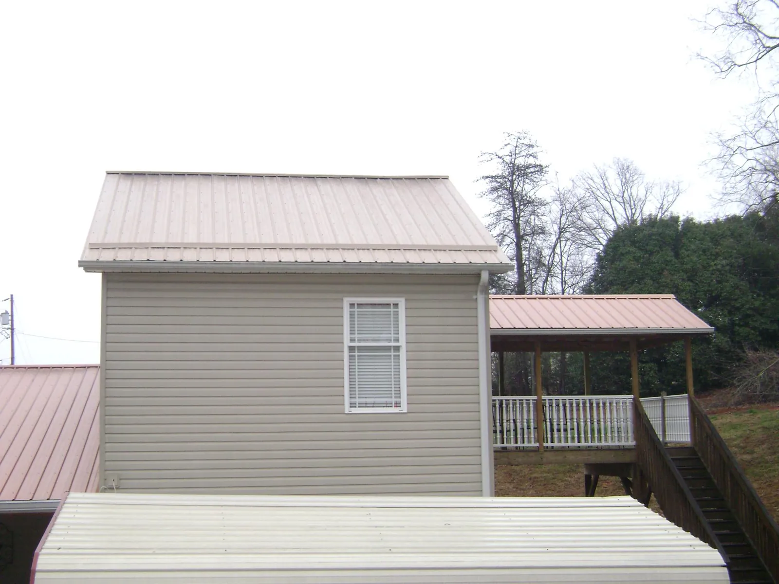 Tan metal roofs on a two story addition and attached porch, from a Roof Replacement job in Lovilia