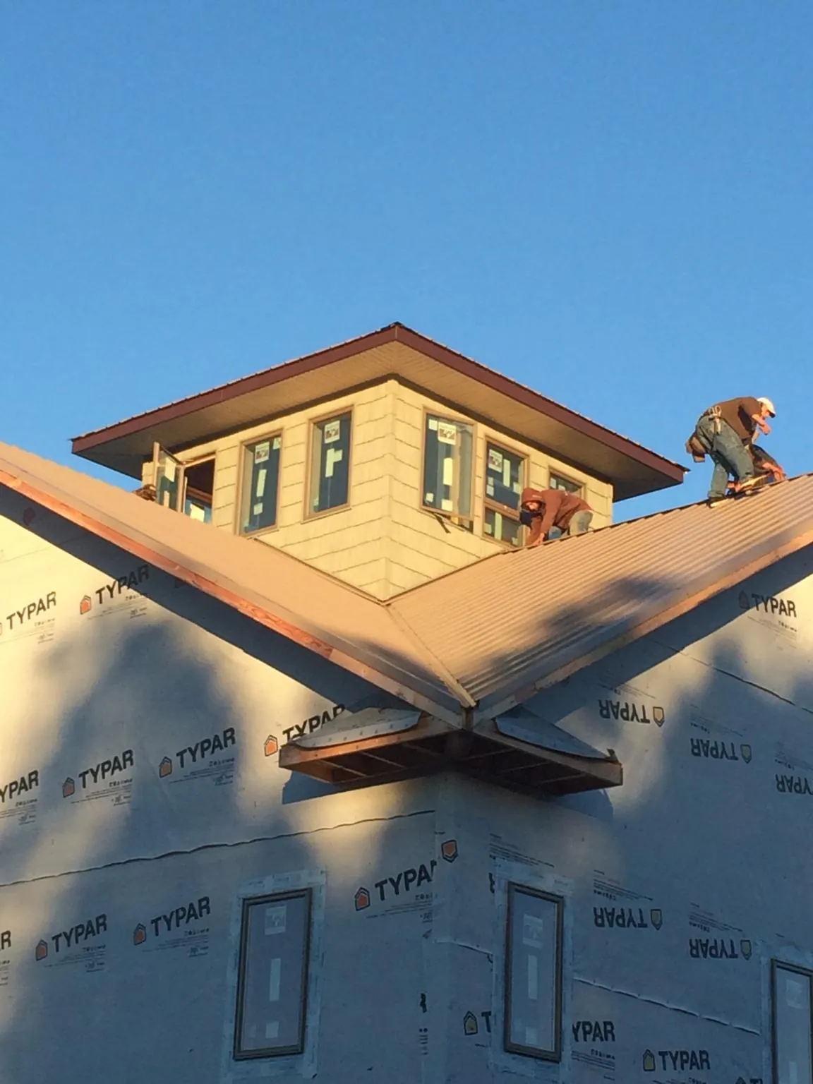 Roofers working around a rooftop cupola on a new metal roof at sunset — Roof Waterproofing in Lovilia by Roofing Brothers
